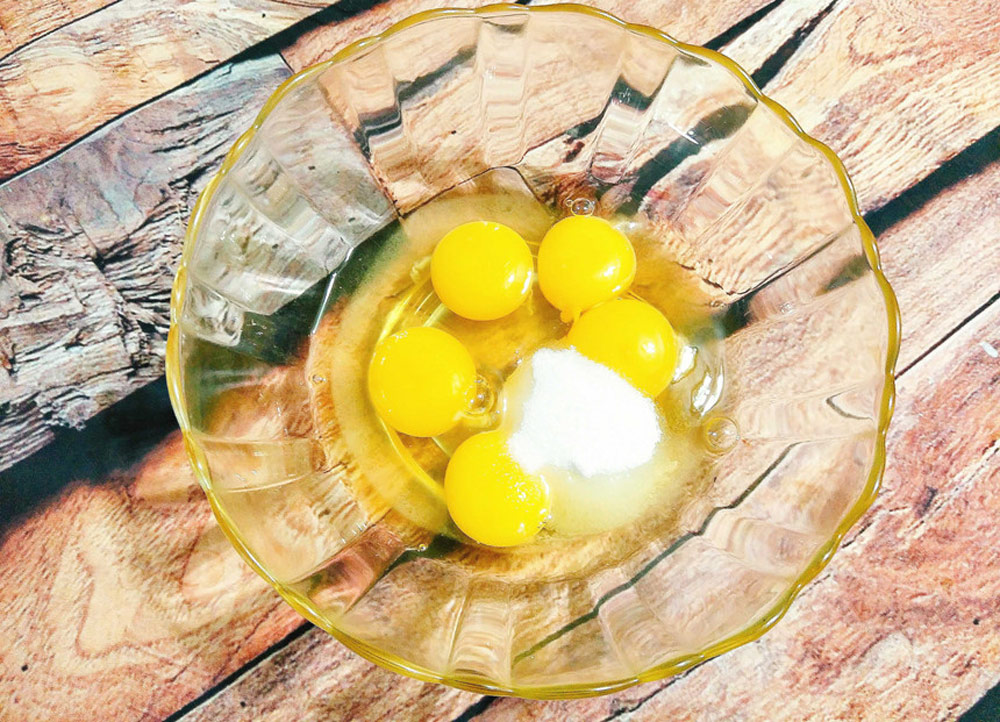 Phần trứng sữa, bạn đập trứng gà ra tô sạch rồi lấy thêm 2 lòng đỏ trứng gà cho vào cùng, thêm 50 gram đường và khuấy đều cho trứng đường tan hết