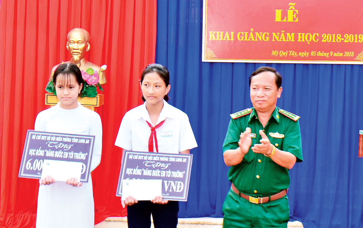 Đại tá Nguyễn Văn Quan -  Chính ủy Bộ Chỉ huy Bộ đội  Biên phòng tỉnh, trao tiền hỗ trợ  từ chương trình “Nâng bước em  tới trường” cho học sinh nghèo huyện Đức Huệ