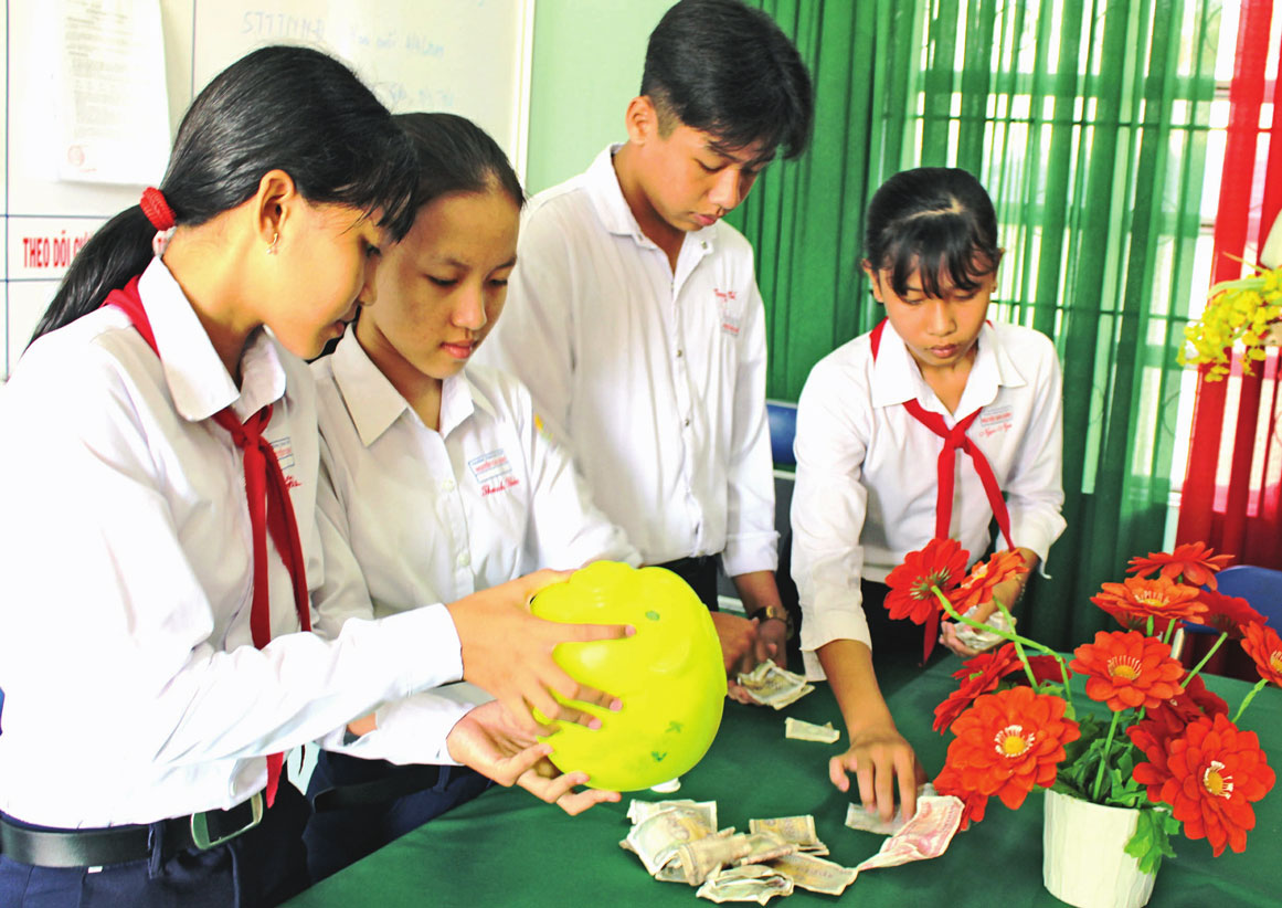 Trương Hoàng Ngọc Nga (bìa phải) cùng các bạn thu hoạch heo đất tiết kiệm giúp đỡ đội viên có hoàn cảnh khó khăn