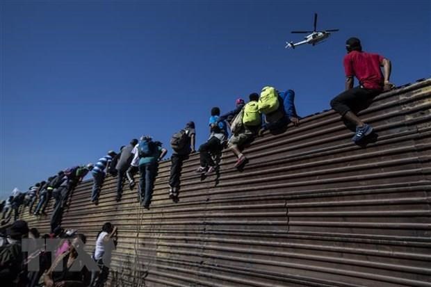 Người di cư vượt qua bức tường biên giới Mỹ-Mexico ở gần cửa khẩu El Chaparral, Tijuana, bang Baja California, Mexico. (Ảnh: AFP/TTXVN)
