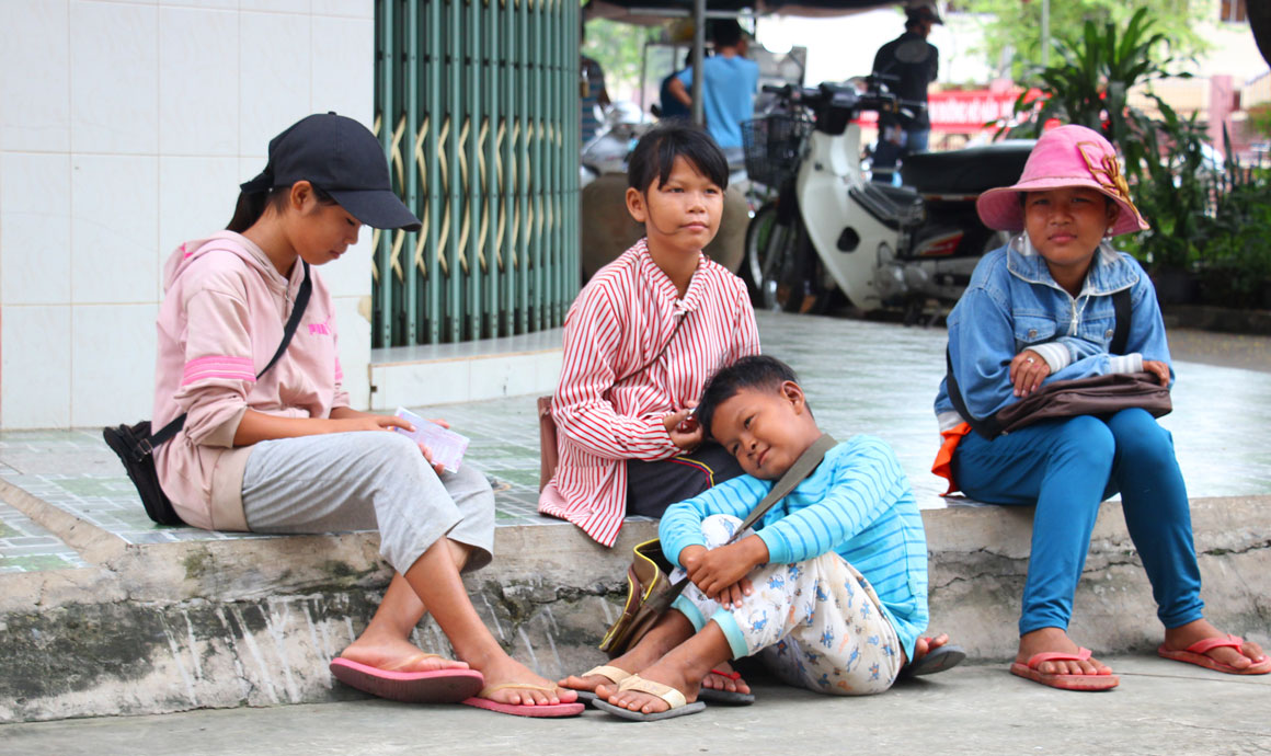 Buổi trưa, những đứa trẻ tìm chỗ có bóng cây, ngồi bệt dưới nền đường nghỉ, dành sức cho buổi chiều