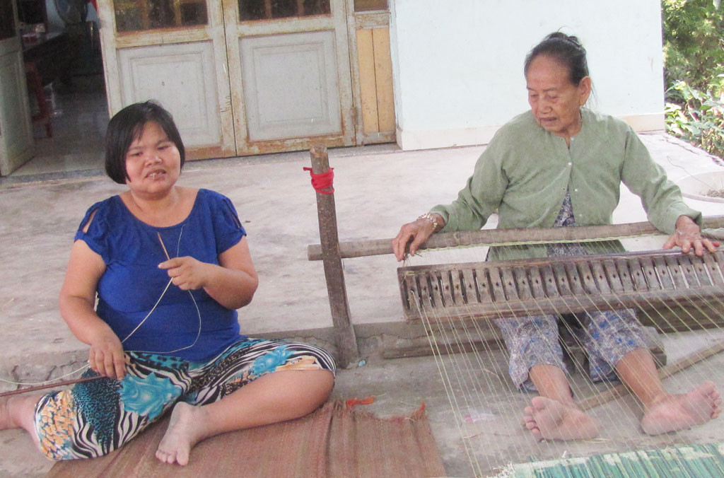 Bà Nguyễn Thị Năm cùng người cháu khuyết tật đang dệt chiếu