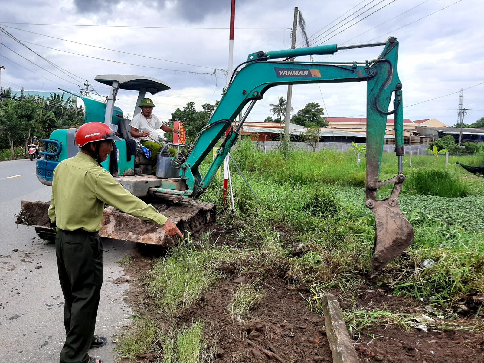 Suốt ngày, chẳng mấy khi ông Trần Văn Xanh có mặt ở nhà, không đi vận động thì đi mời họp, tập huấn, giám sát các công trình đang thi công trong ấp, đôi khi là tăng cường lực lượng phát quang, trồng hoa tại các ấp khác trong xã (Ảnh: Ông Xanh hướng dẫn xe xúc dọn dẹp tuyến đường chuẩn bị trồng hoa chào mừng đại hội)