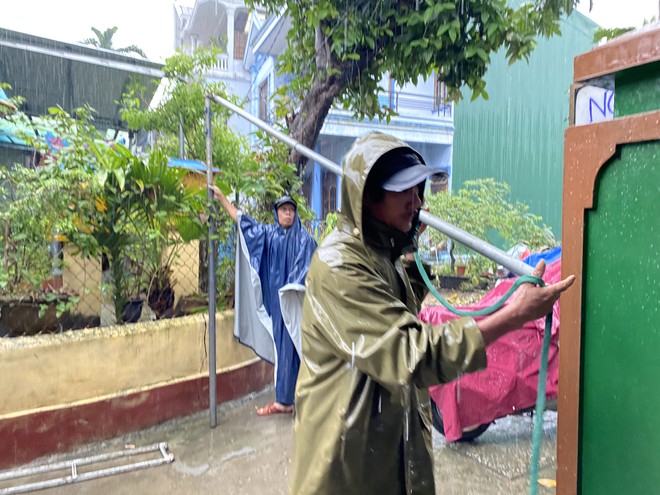 Dưới cơn mưa lớn, nhiều người khẩn trương dựng mái che chờ đưa thiếu tá Phúc về với gia đình. Ảnh: Huy Đạt