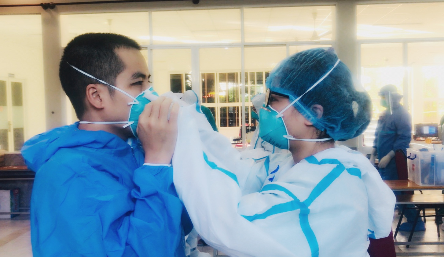 Vợ chồng điều dưỡng Nguyễn Văn Quế và Nguyễn Thị Quỳnh An giúp nhau mặc trang phục phòng hộ trước khi vào ca