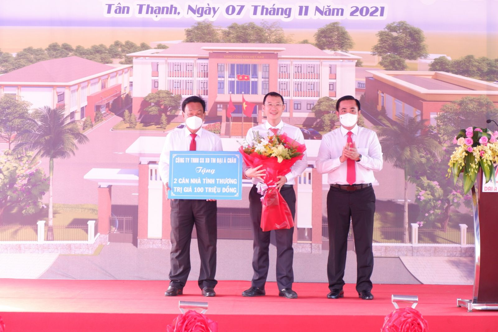 Chairman of Tan Thanh District People's Committee - Le Thanh Dong (R) presents flowers to the representative of Dai A Chau Manufacturing-Building-Trading Co., Ltd. in awarding the amount of 100 million VND to build 2 charity houses 