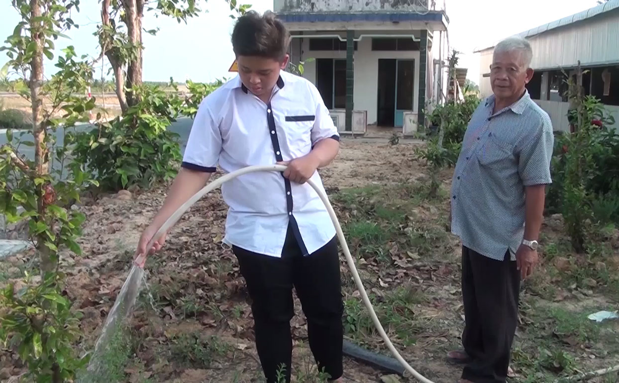 Ông Huỳnh Văn Cọp cùng cháu nội chăm sóc vườn cây của gia đình